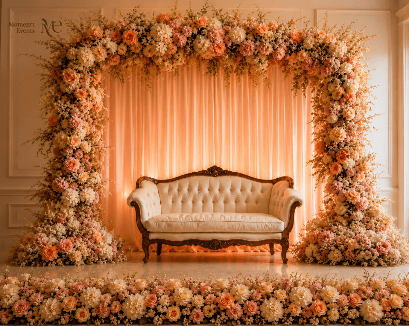 Wedding reception loveseat framed by a peach and cream floral arch, styled by Momentz Events